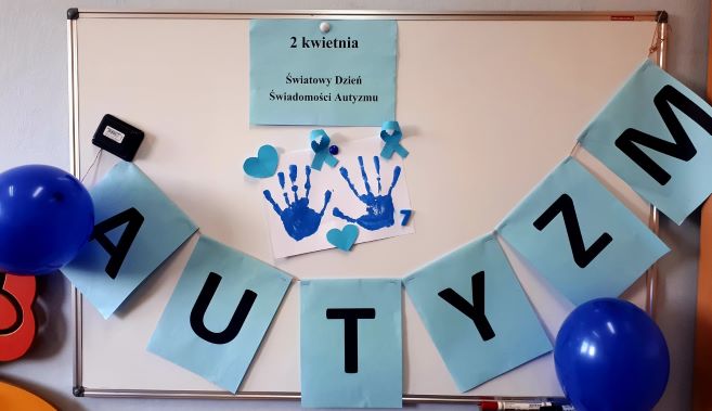 na tablicy umieszczony niebieski napis- autyzm i odbite niebieskie dłonie