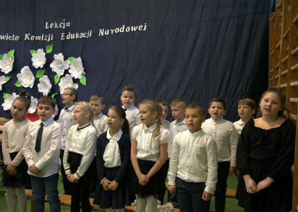 Zdjęcie przedstawia uczniów klasy 2 podczas śpiewania na uroczystej akademii z okazji Dnia Edukacji Narodowej.    