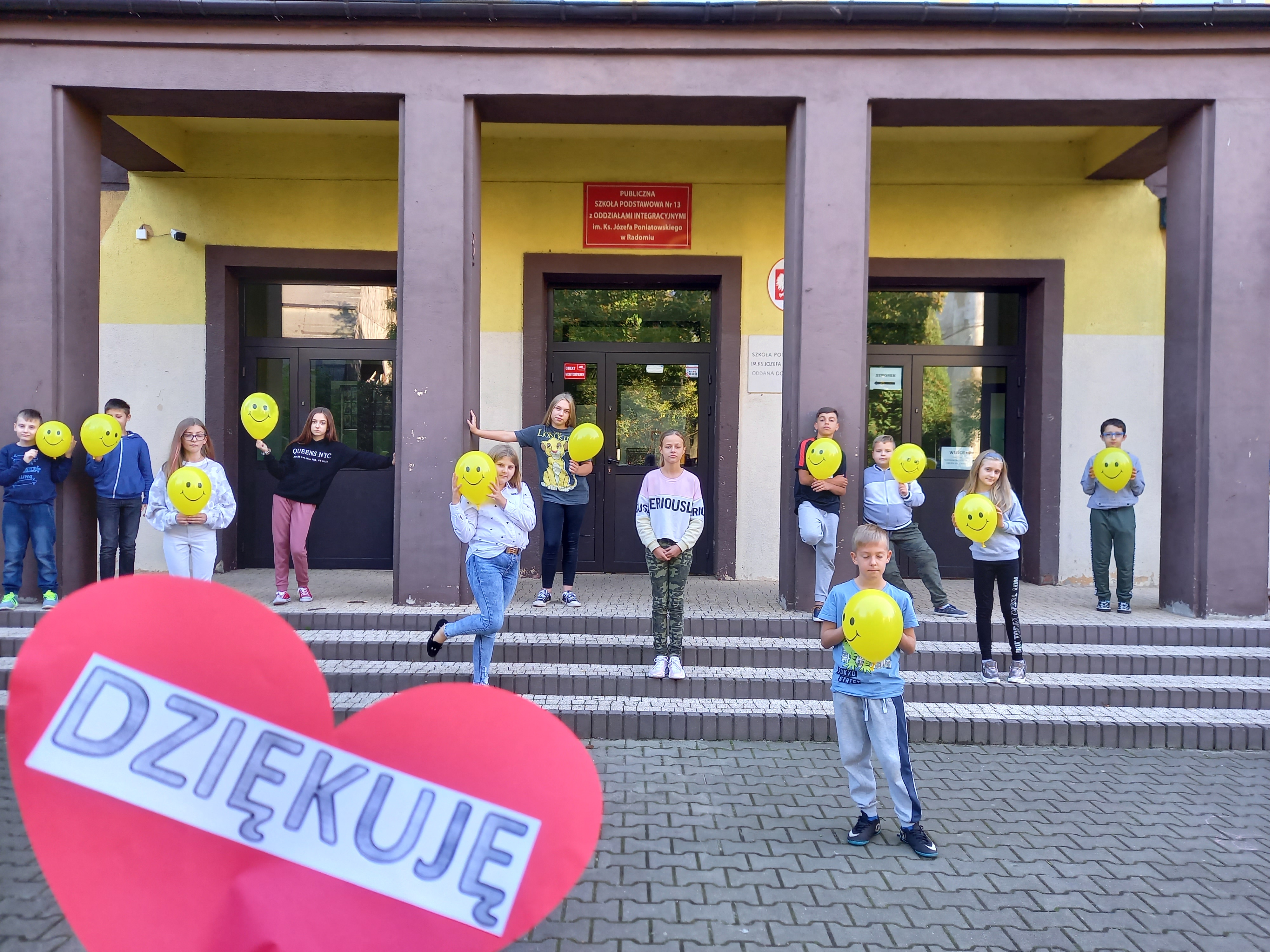  uczniowie stoją przed szkołą z balonami, na zdjęciu serce z napisem dziękuję